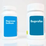 Two generic white plastic bottles of popular over-the-counter pain relievers- ibuprofen and naproxen. Horizontal.